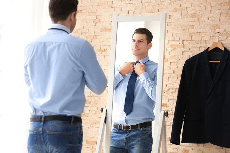 Man adjusting tie before mirror