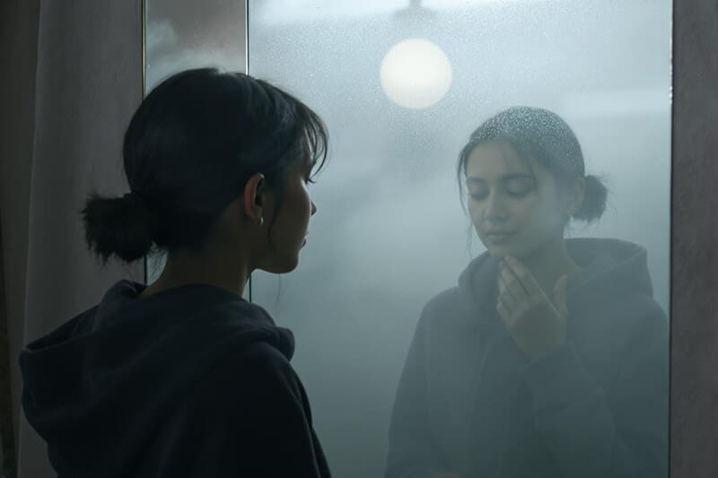 A photo of a woman in front of a mirror with her eyes closed